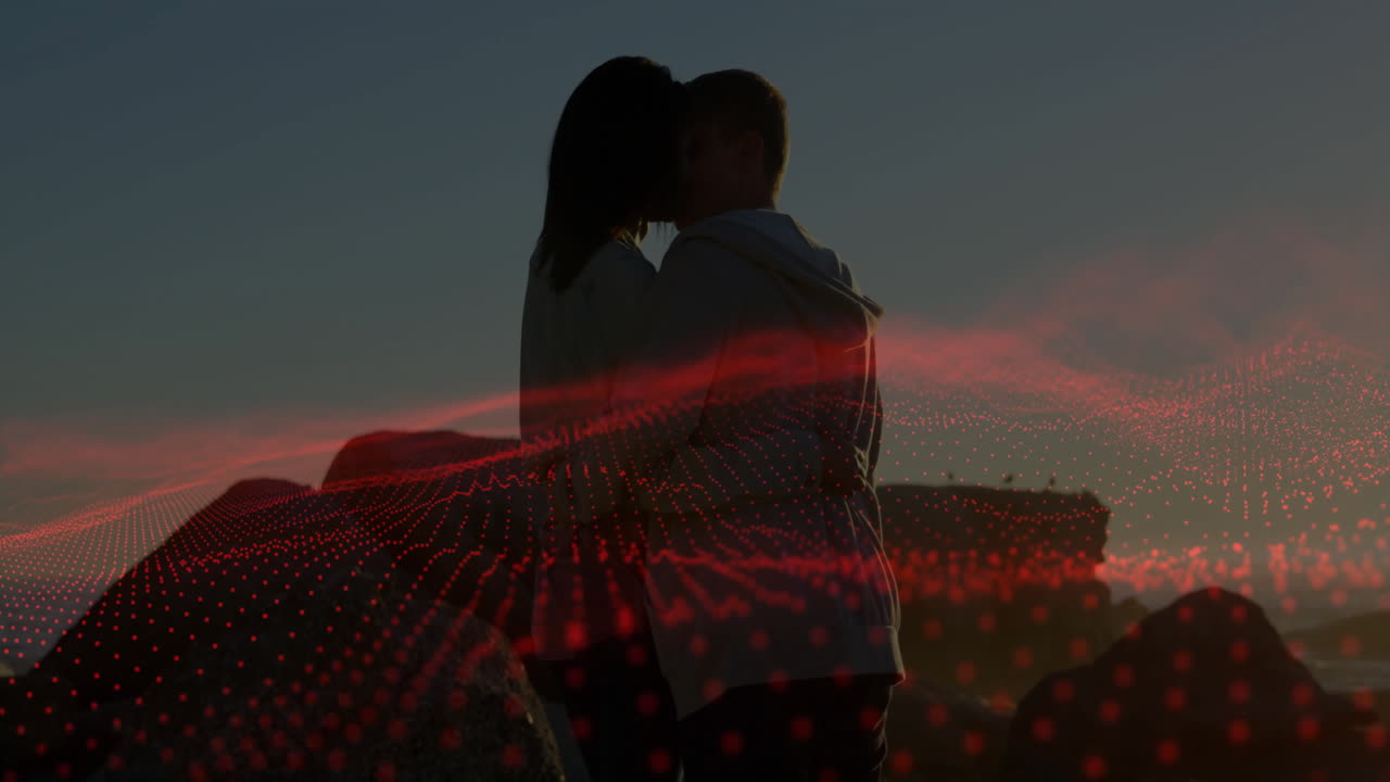Couple kissing on rocky coastline at sunset, with red grid animation showing technology data