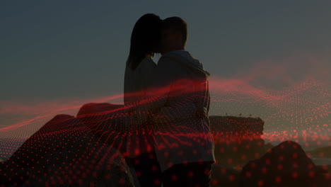 couple kissing on rocky coastline at sunset, with red grid animation showing technology data