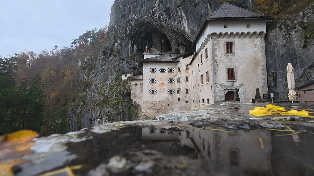 Predjama Castle built within a cave mouth in Slovenia reflecting in a puddle during a cloudy day