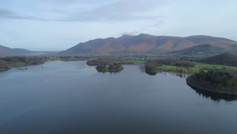 aerial drone shot backwards over derwentwater lake keswick moving away from skiddaw mountain in background on sunny morning with clouds lake district cumbria united kingdom