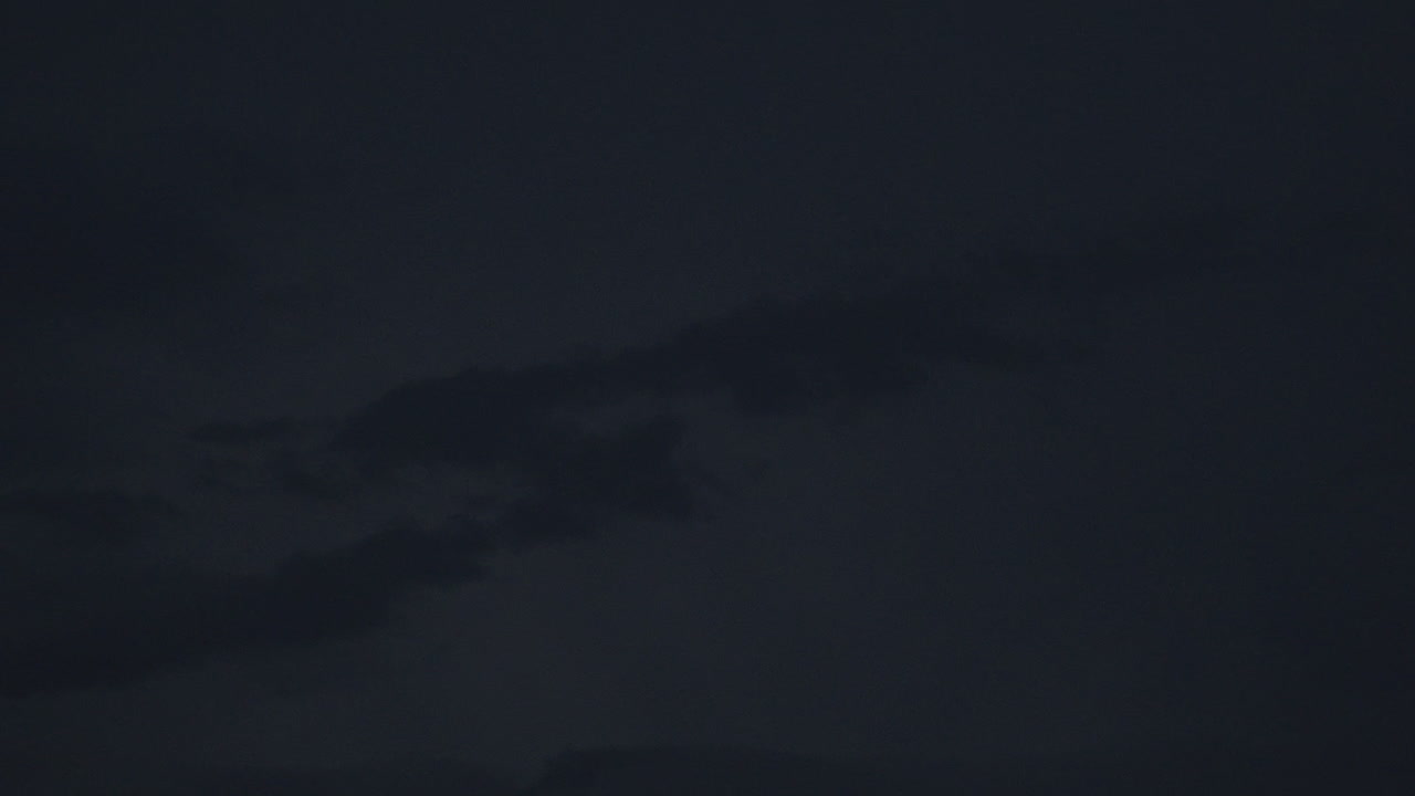 Gentle lightning illuminates dark clouds in the night sky, creating drama