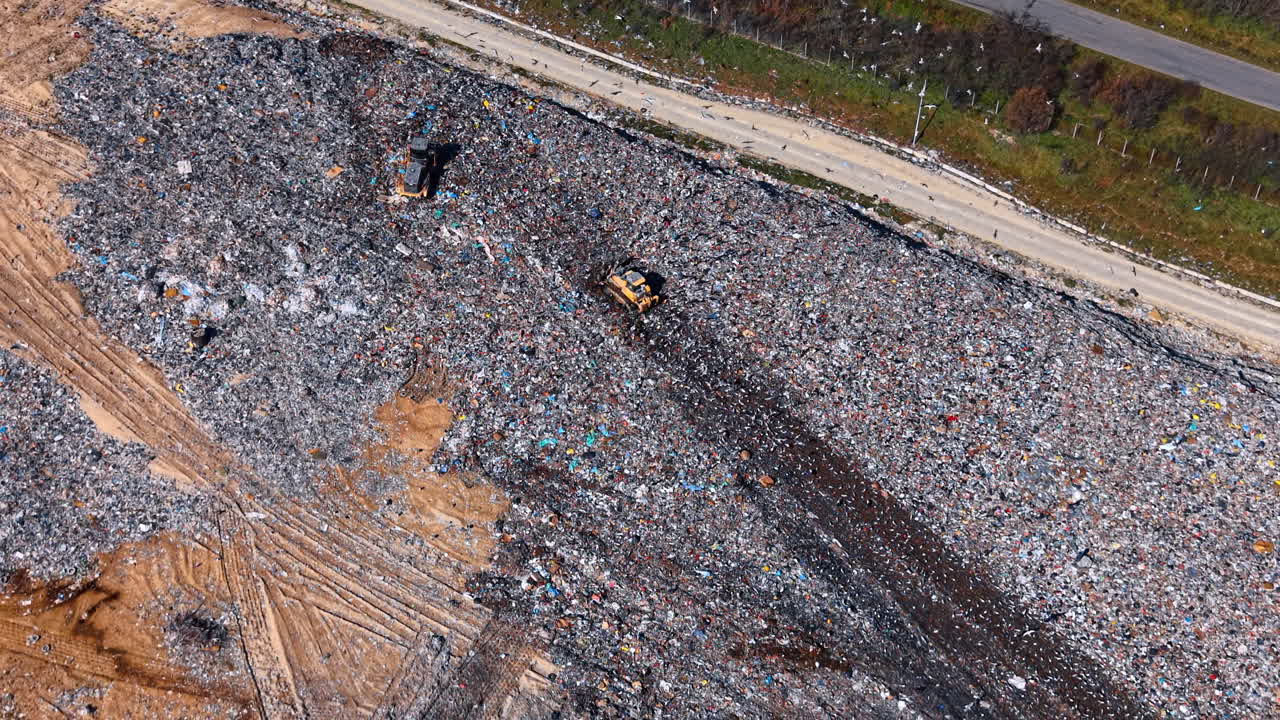 Bulldozer compacting household waste at industrial landfill. Aerial view of a yellow bulldozer moving through a dense pile of trash at a disposal facility