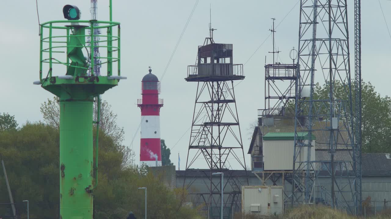 faro de puerto pintado de rojo en el puerto de liepaja en un día nublado, vista lejana, baliza de navegación de puerto verde en primer plano, torres de comunicación, plano medio