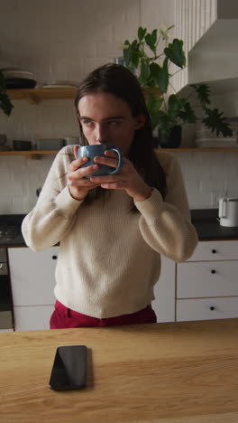video vertical de una mujer transgénero caucásica no binaria bebiendo café en la cocina