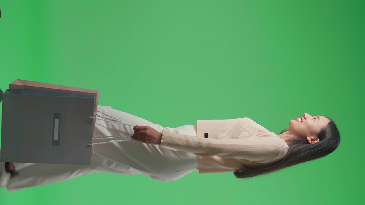 Side View Of An Asian Shopping Woman With Shopping Bags Smile And Walking In Front Of Green Screen