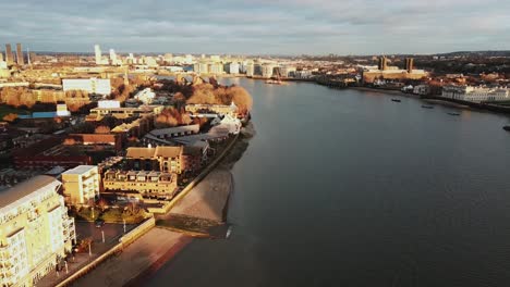 an aerial drone shot over the thames river in london during sunset while waves are reaching to banks