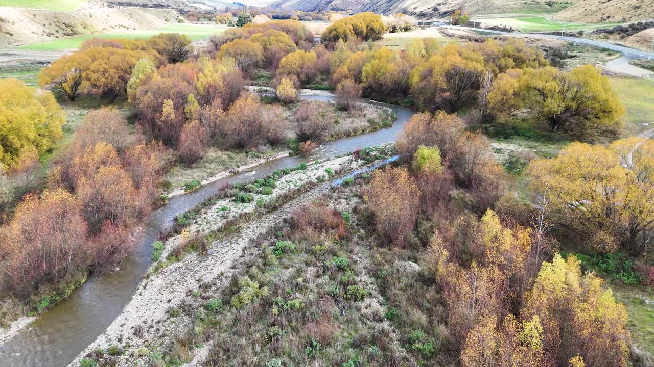 Drone footage captures a winding river surrounded by vibrant autumn foliage in a tranquil landscape