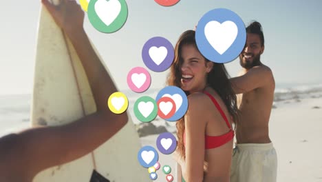 animation of heart digital icons over friends with surfboards on beach