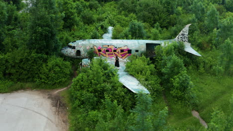 Drone-aerial-pan-shot-as-woman-walks-on-wing-of-old-derelict-craft