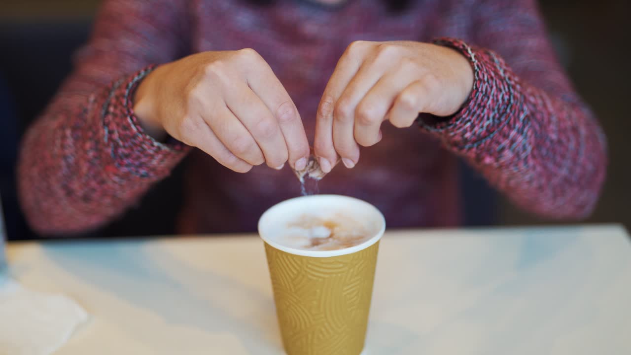 Girl adding sugar to her coffee in a fast food restaurant. Coffee break in cafe