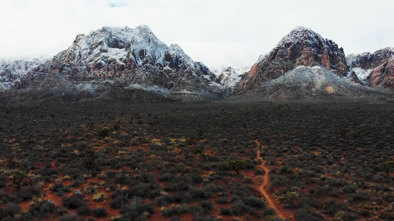 drone aéreo disparado a lo largo de una pista de senderismo con montañas cubiertas de nieve en el fondo
