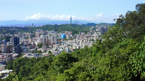 Toma-Aérea-Que-Muestra-La-Hermosa-Ciudad-De-Taipei-Con-La-Silueta-De-La-Montaña-Verde-En-El-Fondo---Torre-101-Que-Se-Eleva-Hacia-Las-Nubes-En-Taiwán---Metrópolis-Asiática