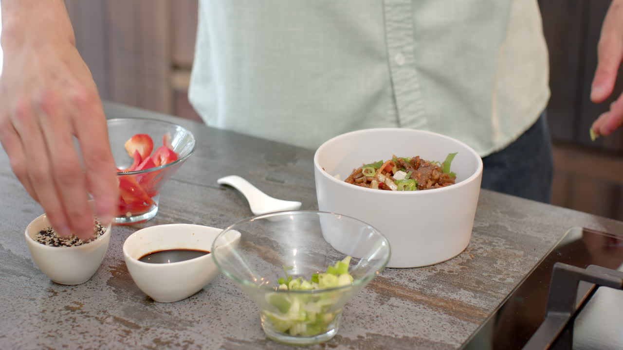 Preparing delicious Asian dish, adding sesame seeds and green onions in kitchen