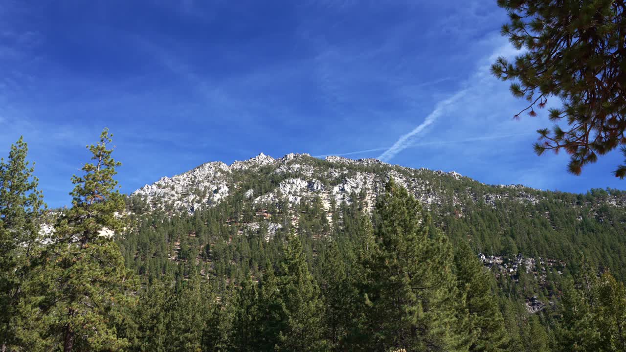 Cielo dinamico sopra una montagna ricoperta di pini con nuvole in movimento.