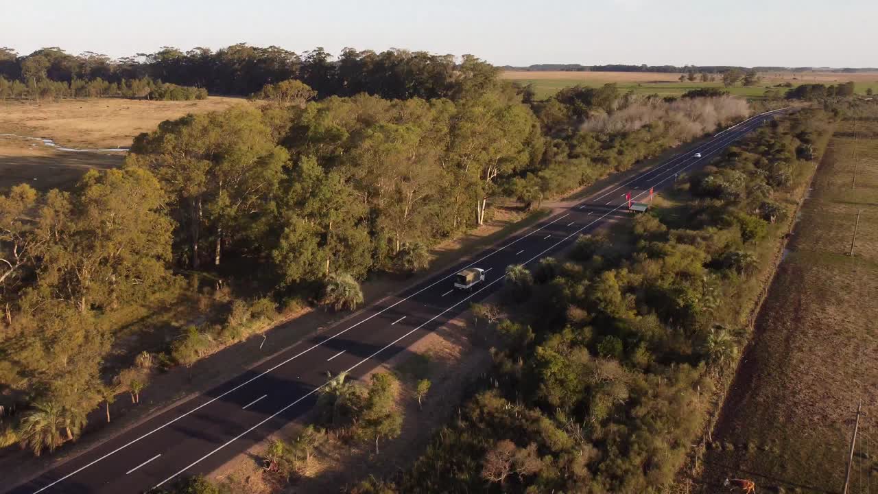 Drone-kuva valkoisesta pakettiautosta ajamassa ohi maaseututiellä auringonlaskun aikaan Uruguayssa, Etelä-Amerikassa.