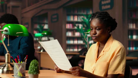 dedicated black student reviewing papers in a traditional library setting