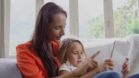 Mother-and-daughter-using-digital-tablet-on-sofa-at-home-4k