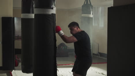 active man engaged in professional boxing in sportswear and gloves hits punching bag in basement of sports club. playing sports and letting out aggression