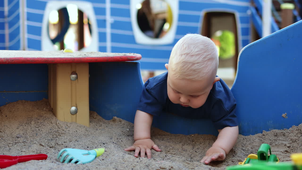 Baby boy playing with sand outdoors. Child development. Children's games on the playground