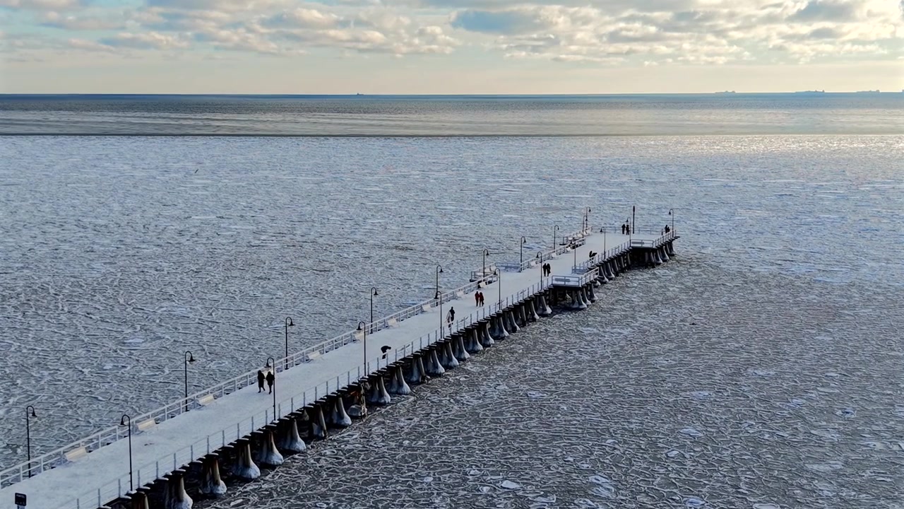 Aerial drone shot of the Orłowo pier reaching out over the frozen Baltic Sea covered with drifting ice on a sunny winter day, Gdynia, Poland