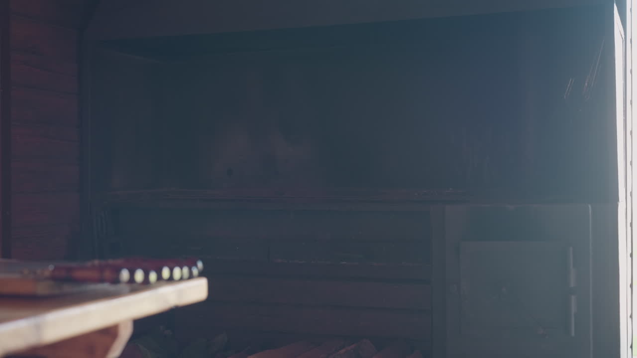 Close up of polished wooden skewers with dark glossy handles arranged on rustic wooden table near indoor barbecue grill in warm cabin interior under soft natural light