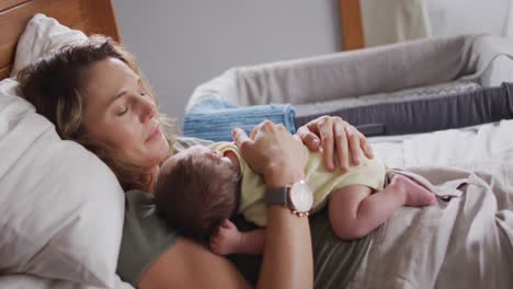 video of happy caucasian mother lying on bed with sleeping newborn baby