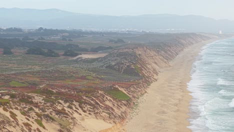 panning aerial shot revealing green dunes, sandy beach, and ocean waves near marina, california