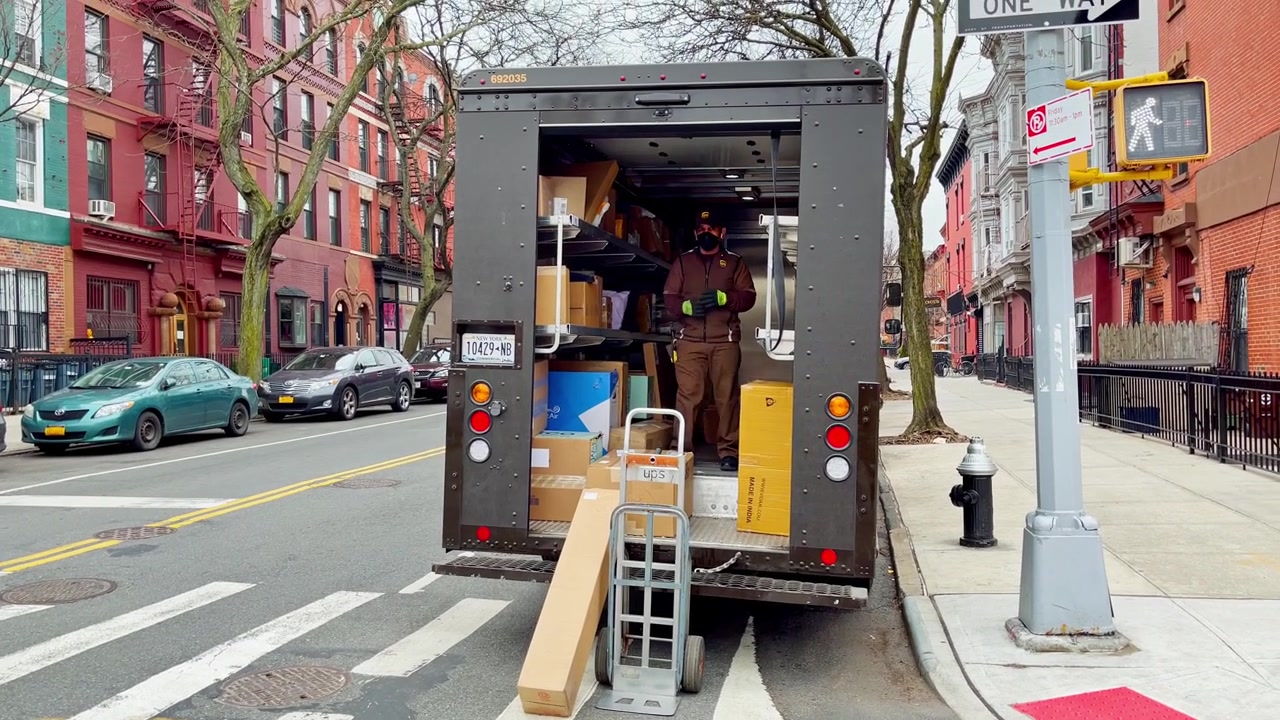 New York, VS, 9 maart 2022: Bezorgkoerier staat in een open transportwagen gevuld met vrachtdozen.