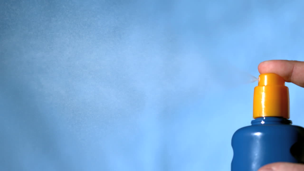 파란색 배경에 손으로 선크림을 스프레이합니다.