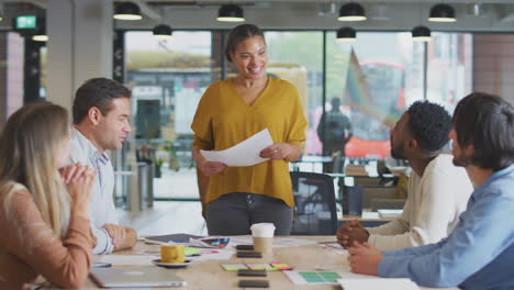 Colleagues-Applauding-As-Businesswoman-Gives-Presentation-In-Modern-Open-Plan-Office