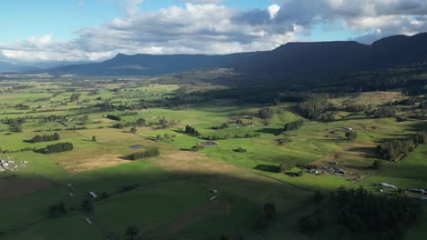 green fields with shadows of clouds and surrounded by mountains, aerial dynamic