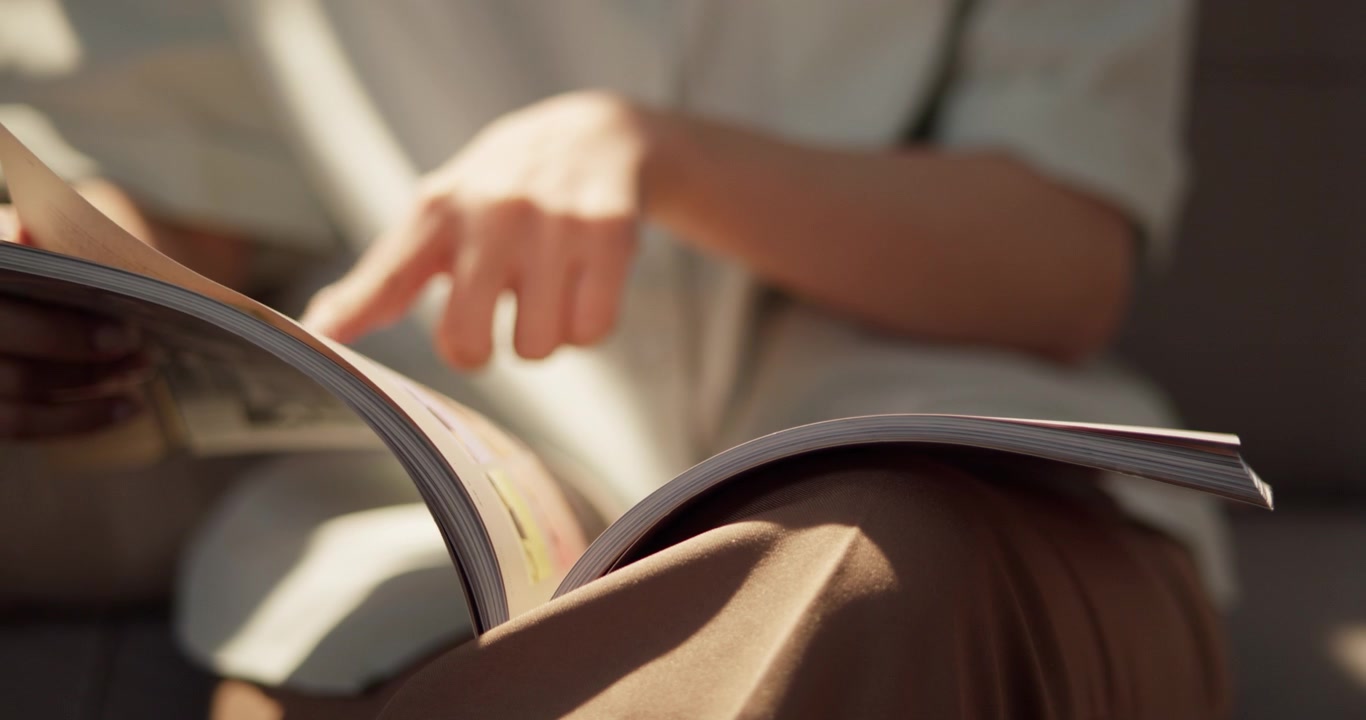 窓から差し込む柔らかな日差しに包まれ、快適なソファでお気に入りの雑誌を読みながら、当然の休憩を楽しむ女性の至福のひととき
