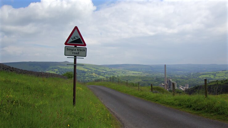 Strada a carreggiata unica con segnale di forte pendenza in un paesaggio di valle rurale.