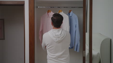 indecisive man looking at his longsleeves shirts hanging on the cloth rack