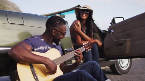 Hombre-Afroamericano-Tocando-La-Guitarra-Para-Su-Novia-Mientras-Está-Sentado-En-La-Carretera