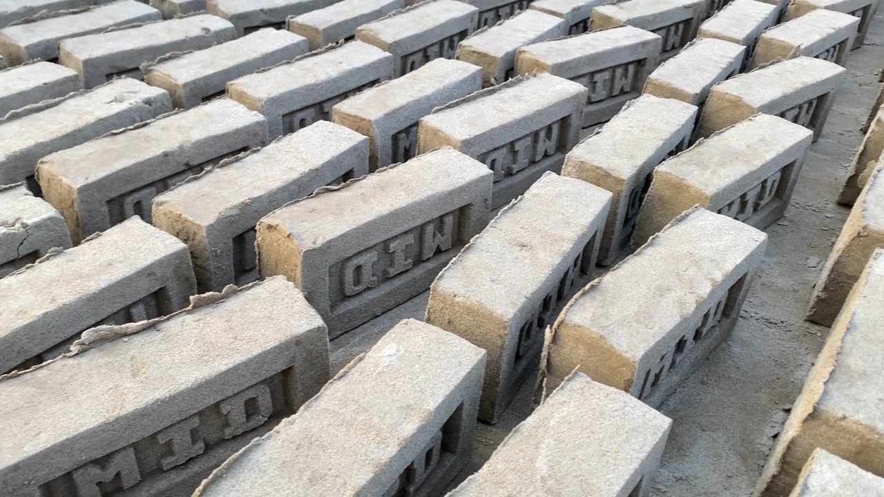 Rows of rectangular raw bricks kept for drying in Bangladesh with raised lettering stand closely packed on a dusty surface under natural light.
