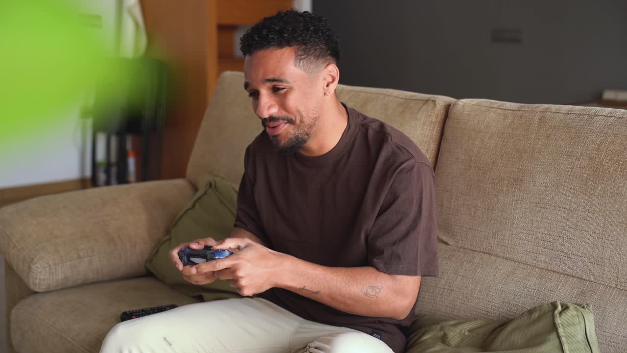 편안한 민족 남자가 침대에서 비디오 게임을 하고 있습니다.