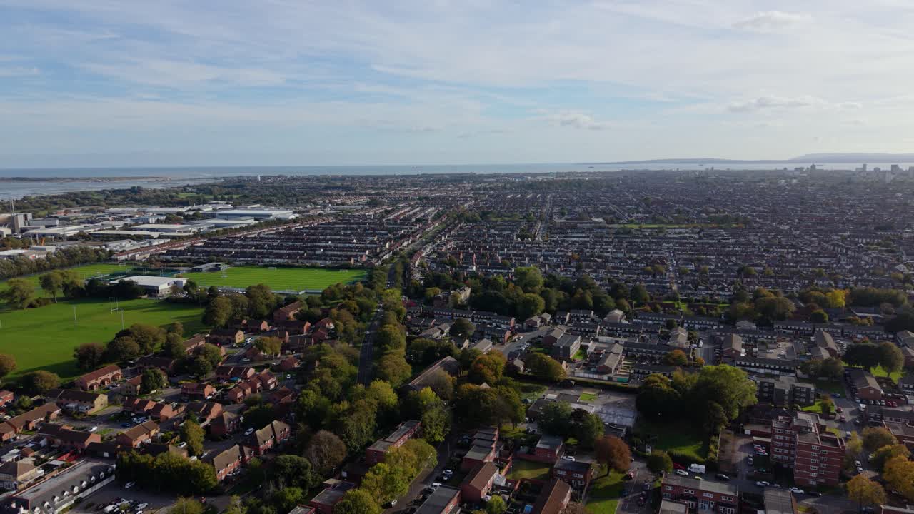 Vol de drone lent, en hauteur et en cercle arrière au-dessus du paysage urbain varié de Portsmouth, Royaume-Uni, incluant terrains de sport, espaces verts, maisons mitoyennes et bâtiments commerciaux, avec vue sur la mer et le port.