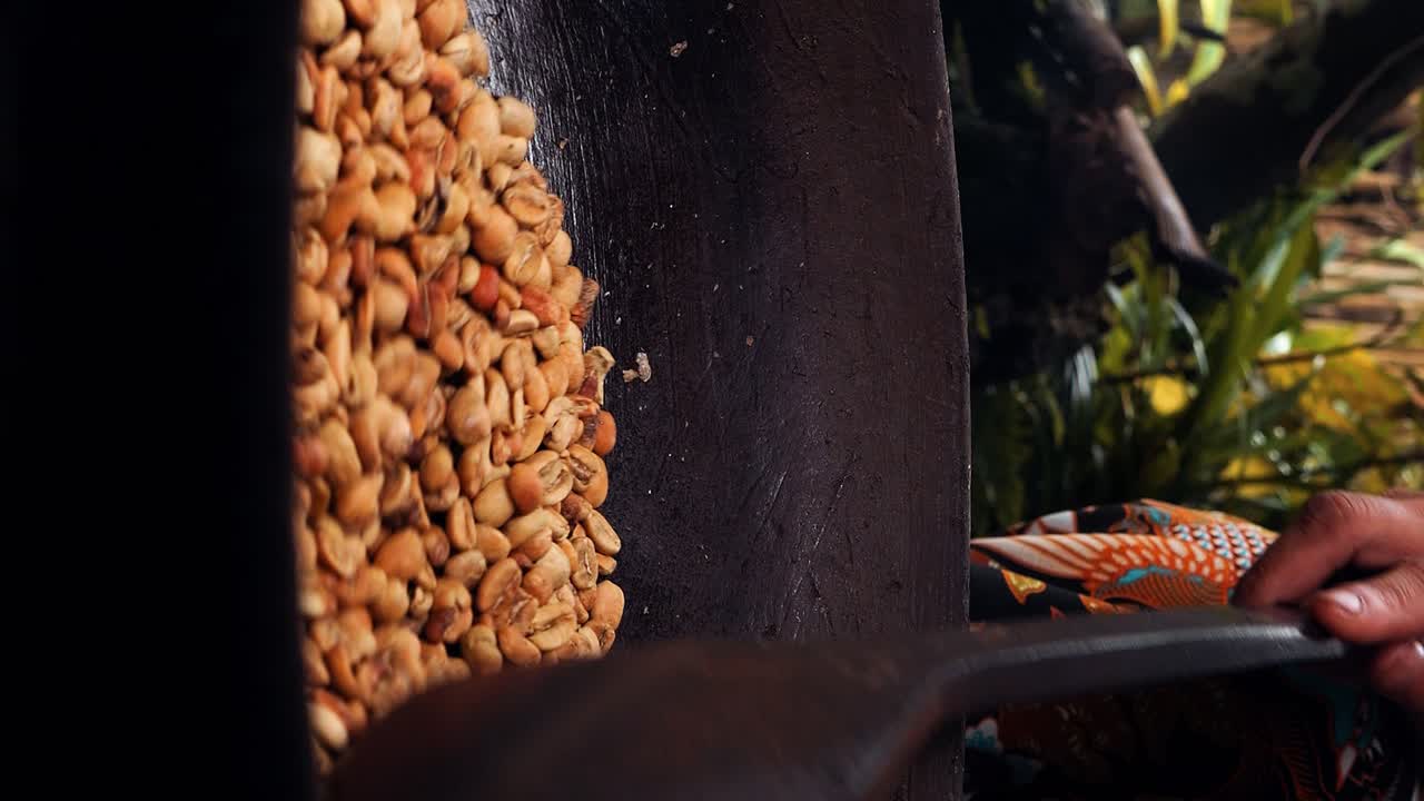 Vertical Medium slow motion shot of roasted coffee beans kopi luwak while the beans are stirred and roasted in a wok with a wooden spoon by one of the coffee plantation's employees in Bali indonesia