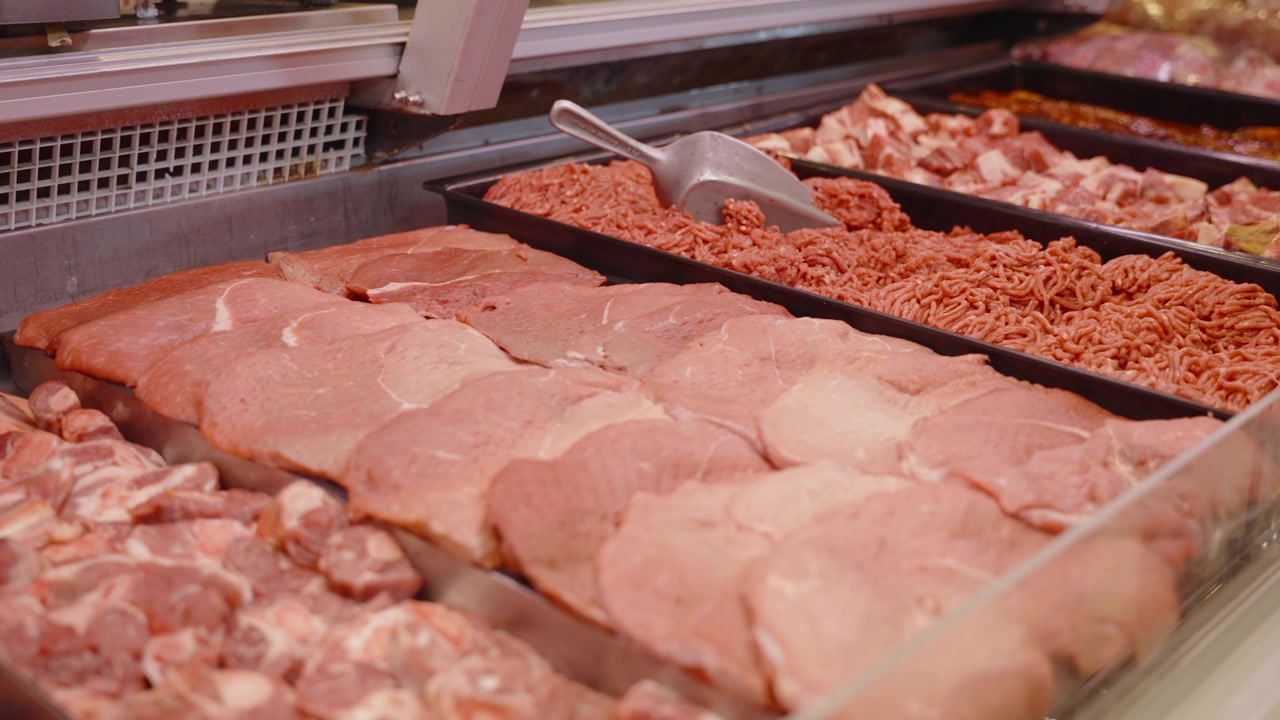 Rows of sliced cuts and ground mince fill metal trays in a retail butchery counter under glass.