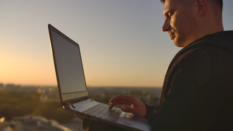 Hipster-man-with-a-laptop-on-the-edge-of-the-roof.-Freelancer-at-work.-Wireless-mobile-Internet.-He-works-on-the-Internet.