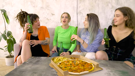 friends laughing and talking while holding beers on a party with pizza