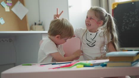 Active-siblings-dance-and-clap-sitting-at-desk-in-playroom