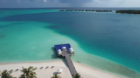 aerial view of luxury resort in maldives with palm trees on beach and overwater infinity pool with bungalows in background