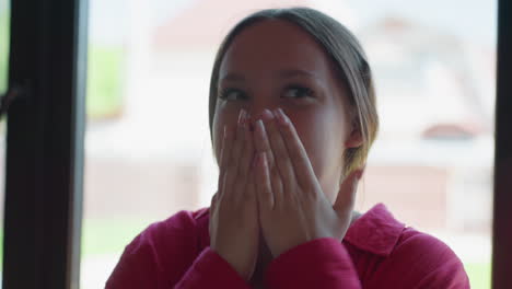 lady in red shirt shyly covers mouth with hands, reacting with playful and expressive face while interacting with unseen people in background, bright indoor light adding warmth to candid moment