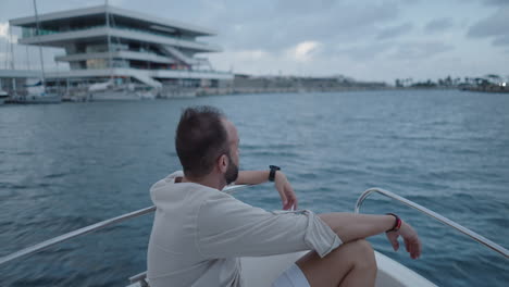 Man sitting on a boat in a marina looking at a modern building
