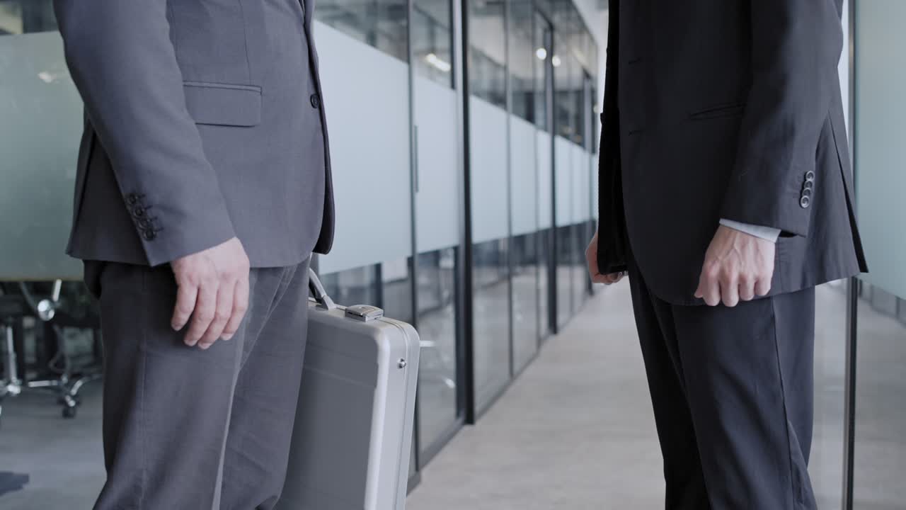 Man in suit passing case to partner in company office, business handshake, deal