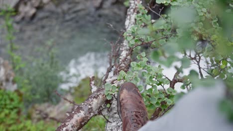 Man-In-Brown-Boots-Standing-At-Tree-Branch-With-River-Below-In-Norway