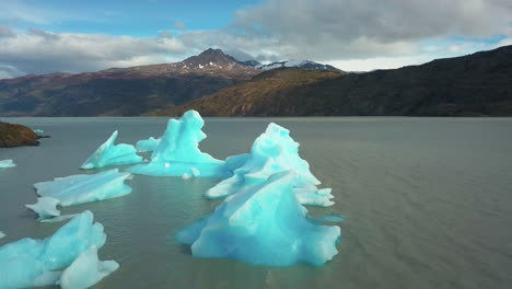 Aerial-drone-view-flying-over-icebergs-floating-in-a-lake-in-the-stunning-mountains-of-Patagonia,-Chile
