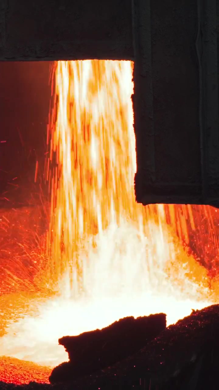 Cascata di metallo fuso che si riversa nella siviera sotto il bordo pesante del forno, flusso ad alta portata con bagliore luminoso del metallo fuso